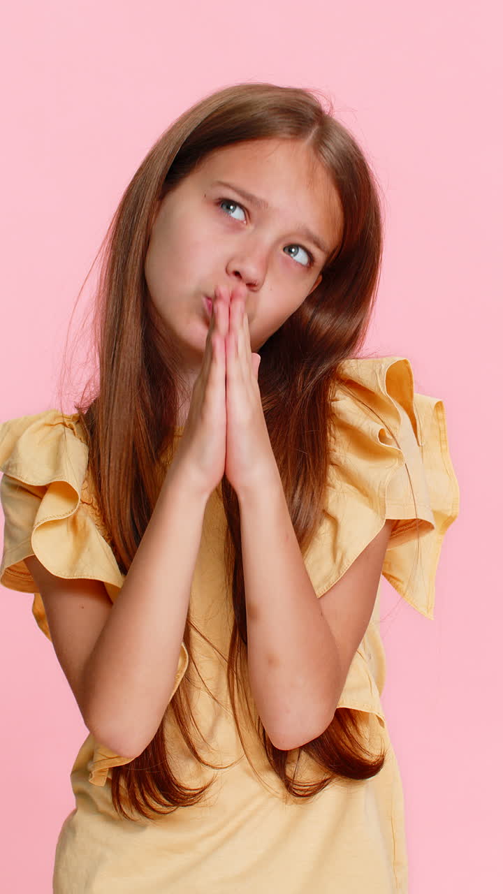Menina com as mãos postas em oração, olhando para cima como se desejasse ou pedisse ajuda ou apoio.