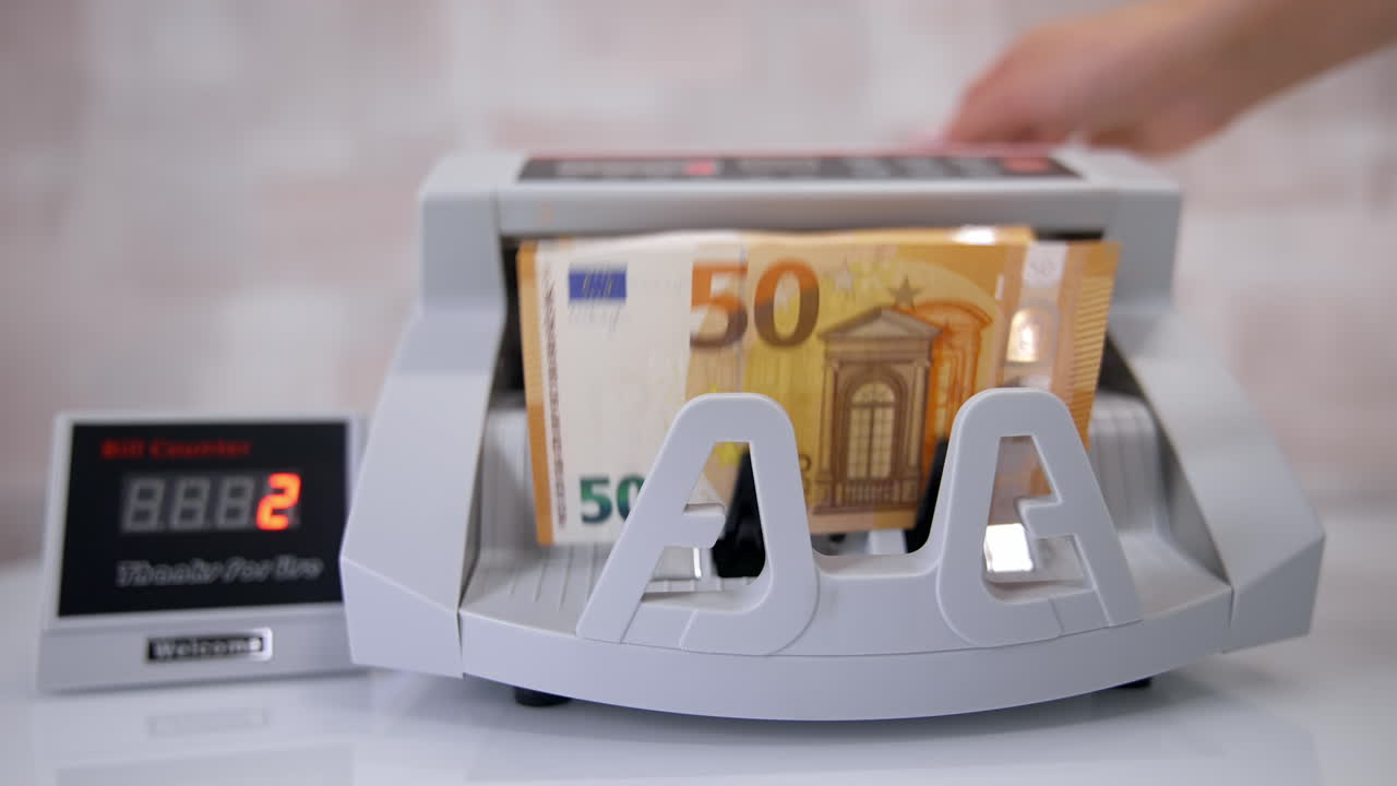 Woman putting money into counting machine at table indoors, close up.