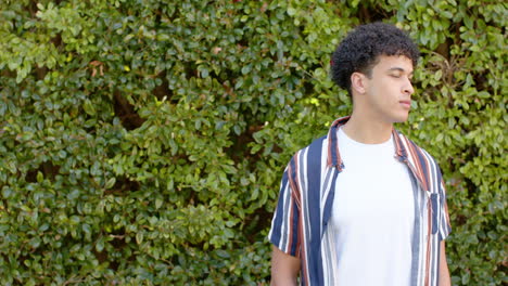 biracial man standing in front of hedge outdoors, slow motion, copy space