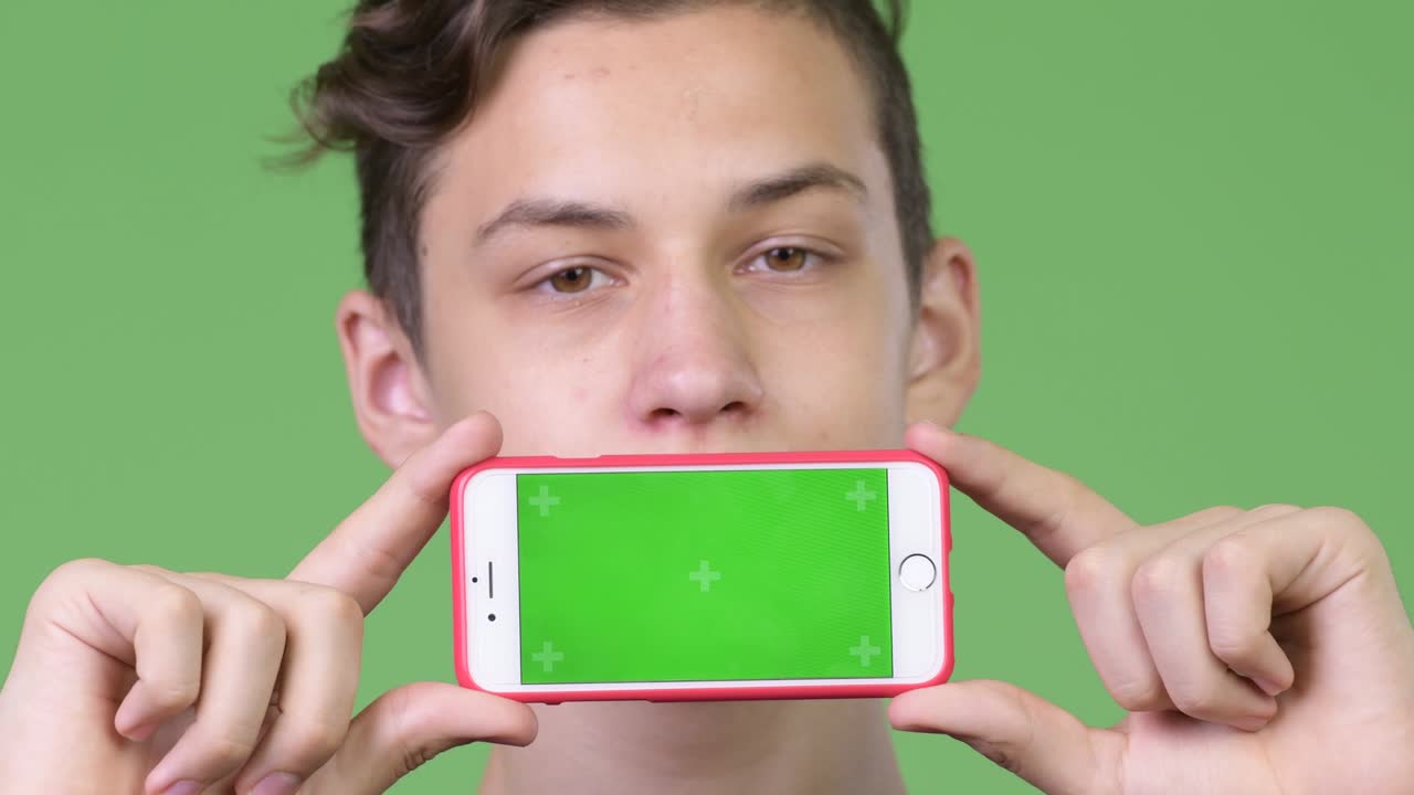 젊은 잘생긴 십대 소년이 전화를 보여줍니다.