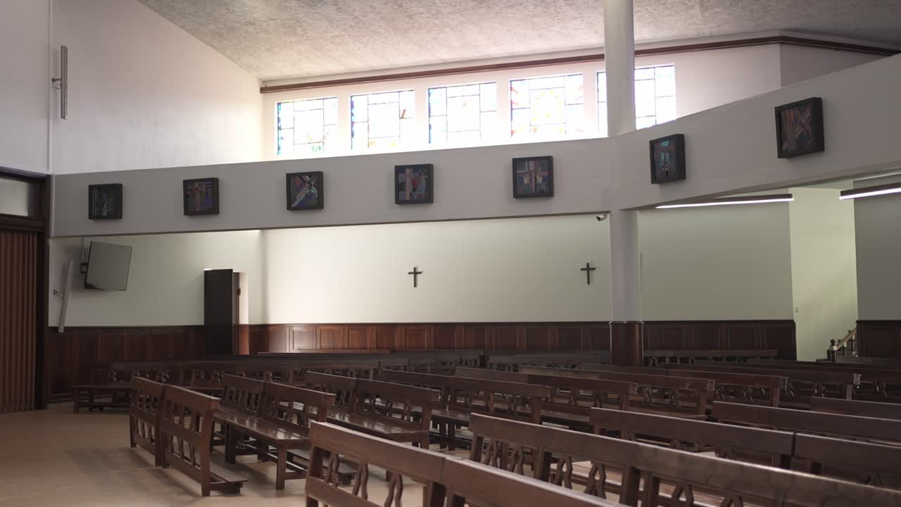 Szeroki widok na pustą salę kościelną z drewnianymi ławkami i krzyżami na ścianach