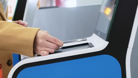 mujer blanca con la mano aplicando un billete de papel a la pantalla de la puerta automática en el aeropuerto. impresión de la tarjeta de embarque en el mostrador de facturación sin contacto antes del vuelo. escáner de código qr usando en la entrada de la terminal de transporte