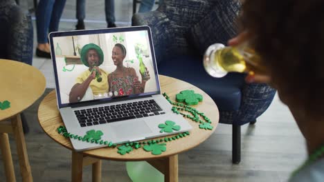 hombre tomando cerveza en una llamada de video portátil celebrando el día de san patricio con amigos