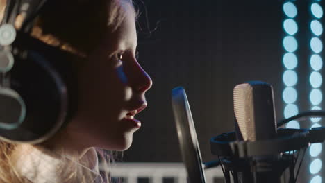 niño sonriente canta en un estudio de audio de primer plano. niña encantadora cerca del micrófono practicando sonidos. niño demuestra habilidades vocales en el estudio de la discográfica