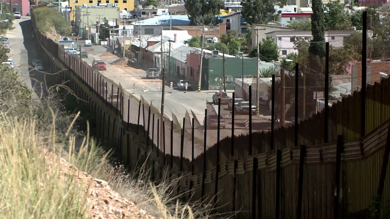 una vista frontal de la ladera detrás de una gran cerca que mira hacia abajo en un vecindario de calles interurbanas