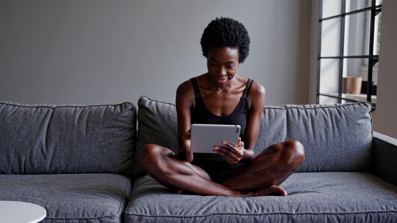 A woman sits on a sofa using her phone, partially obscured by green leaves in the foreground