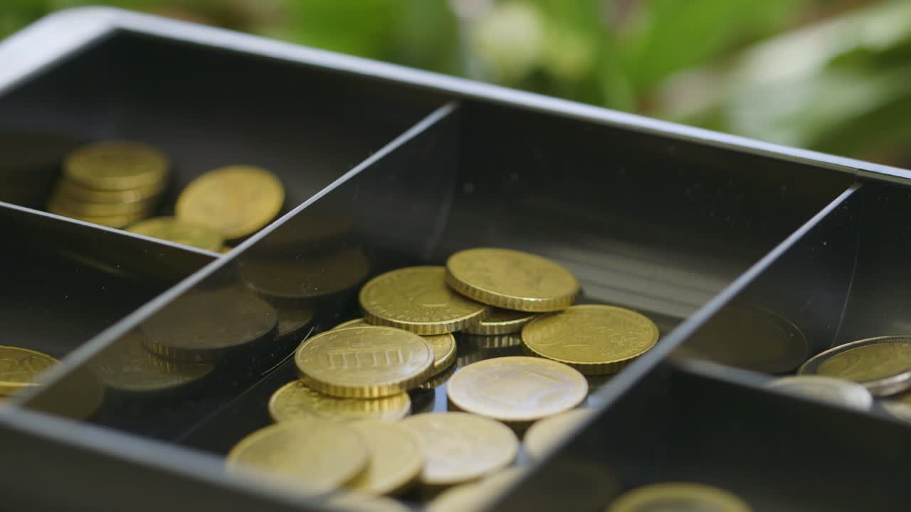 Close-up of a hand taking coins out of a cash register drawer
