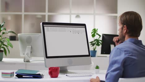 Caucasian-man-sitting-at-desk-watching-coding-data-processing-on-computer-screen