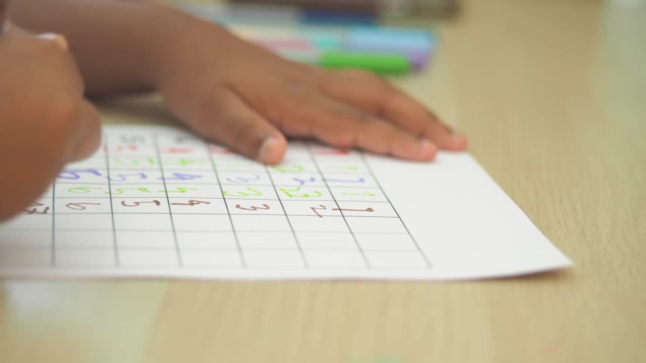 Child's Hands Writing Numbers on a Grid Paper