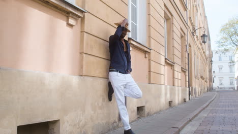 Afro-Caribbean-Man-Putting-His-Panama-Hat-On-While-Leaning-On-The-Wall-With-One-Leg-Up-In-The-Old-Town-Street