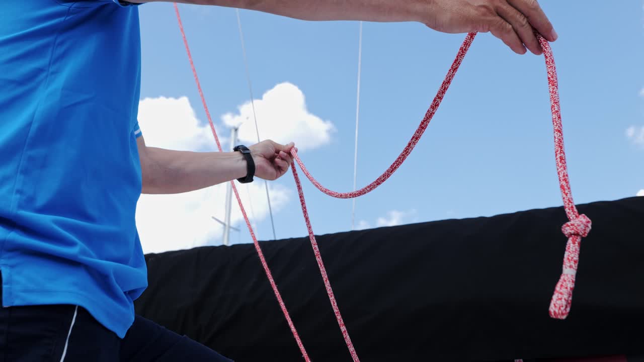 Bright summer day scene showing sailor on deck holding red rope with loose knot