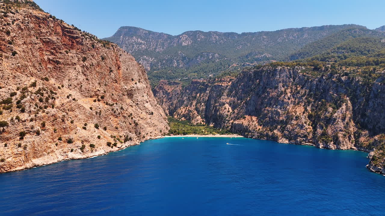Breathtaking cliffs and calm water. Cliffs encircle a serene bay, sunlight sparkling on blue waters and green hills in the background