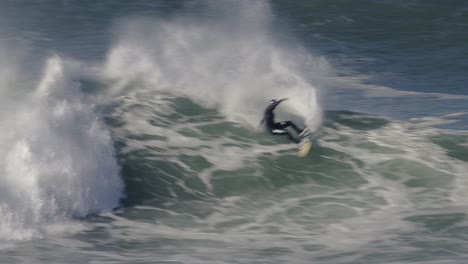 A-surfer-in-a-black-wetsuit-repeatedly-rides-to-the-top-of-a-wave,-where-he-turns-sharply