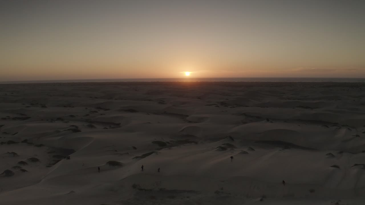 puesta de sol en el horizonte mientras la gente explora las dunas de arena de baja california sur, antena