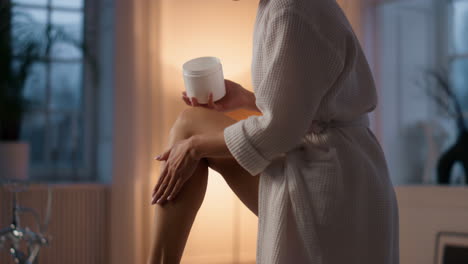 gorgeous woman moisturizing legs at bath closeup. lady putting cream at evening