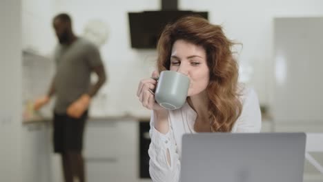 Mujer-Sonriente-Viendo-Noticias-Divertidas-En-La-Computadora-En-La-Cocina-Abierta.