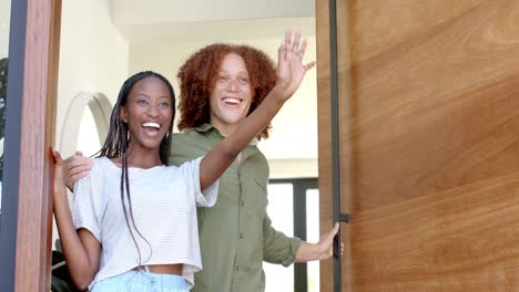 happy diverse couple greeting male friend with wine at front door of home, slow motion