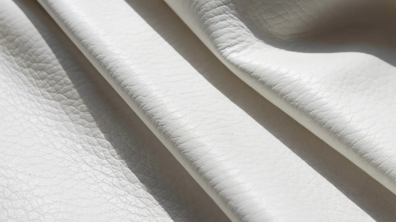 Měnící se světlo vrhající odlesky na detail koženého panelu, odhalující sbíhající se záhyby.