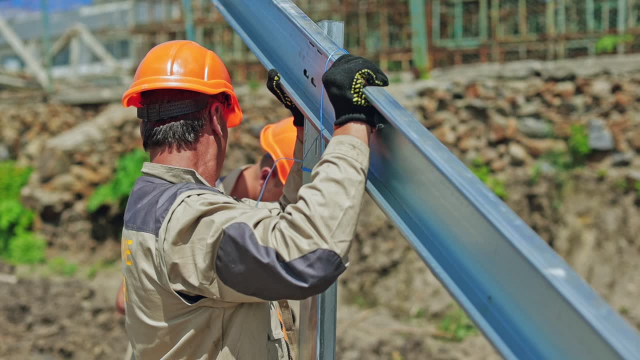 Solar panel technicians install metal frame. Workers in orange helmets making metal basis for solar system on the field. Close-up.