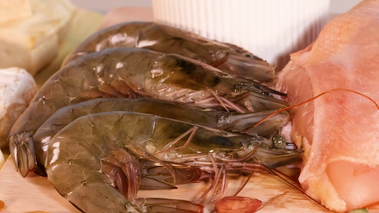 Close-up of shrimp, chicken slices, and assorted nuts on a wooden surface.