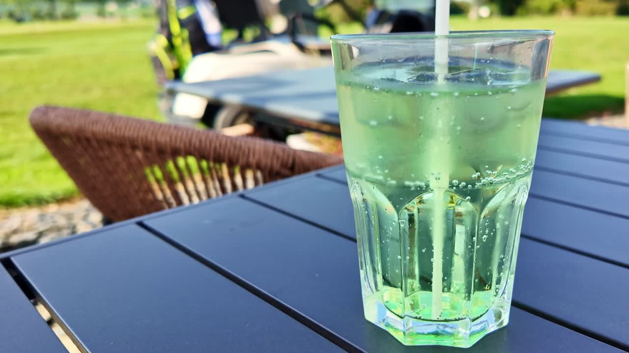 Green kiwi banana soda in glass on outdoor table under natural daylight, effervescent bubbling
