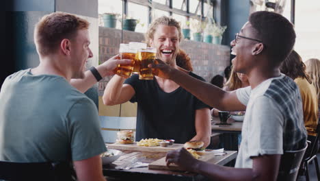 Drei-Junge-Männliche-Freunde-Treffen-Sich-Zu-Getränken-Und-Essen-Und-Stoßen-Im-Restaurant-An