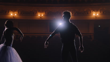 hombre en traje de entrenamiento levanta a la bailarina en sus brazos y gira a su alrededor en el escenario del teatro. par de bailarines de ballet clásico en el ensayo antes de la actuación. sala teatral iluminada. cámara lenta.