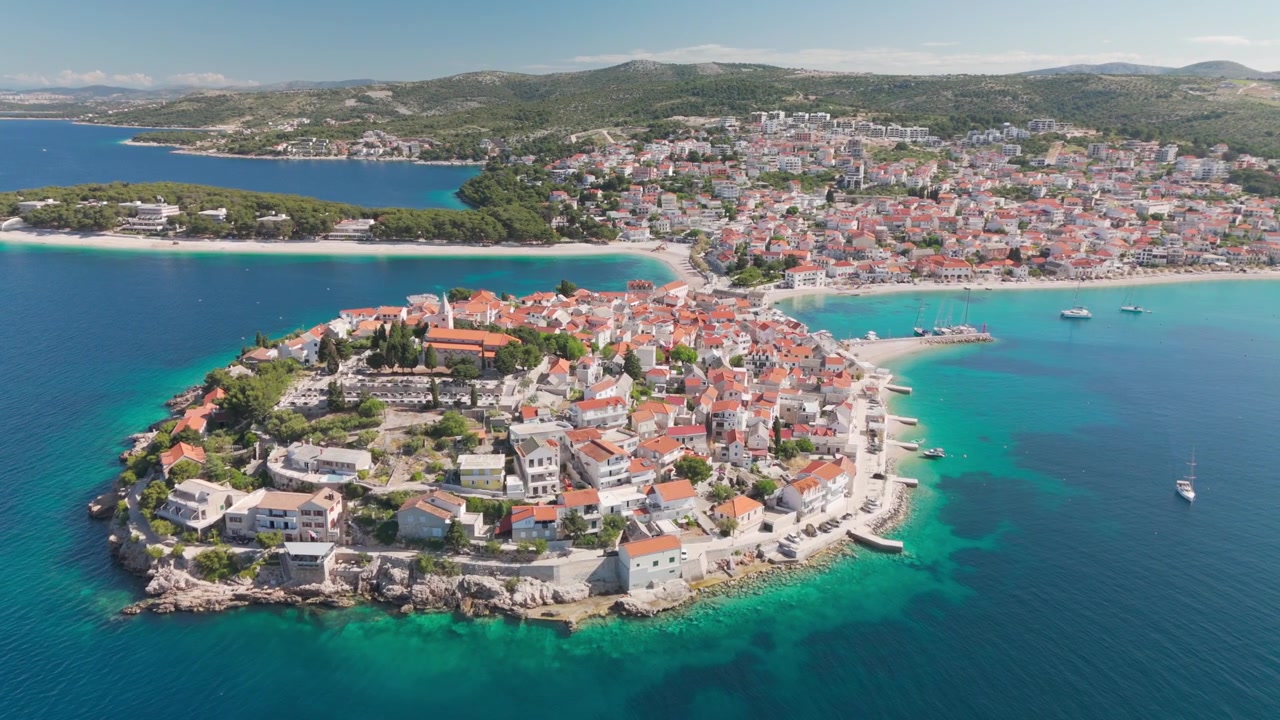 Drone, Primošten'in eski şehir yarımadası etrafında deniz tarafından yarım daire çizerek dönüyor, parlak Adriyatik üzerinde kilise kulesini ve kıyı şeridini görüş alanında tutarak