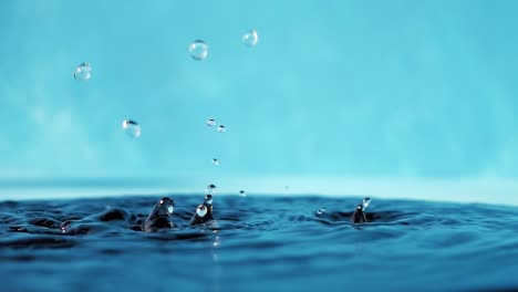vídeo en 4k en cámara lenta de una superficie de agua con gotas que caen sobre un fondo azul. salpicaduras de agua. rodaje de estudio.