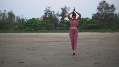 chica india de gimnasio al aire libre, se calienta con la rutina de ejercicios de manos rezando en la playa