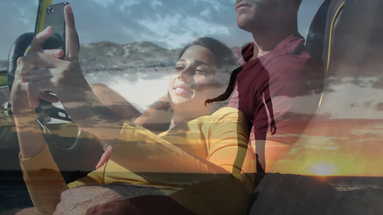 Di dalam mobil, pasangan menonton animasi dengan overlay matahari terbenam dan pantai, bersantai bersama.