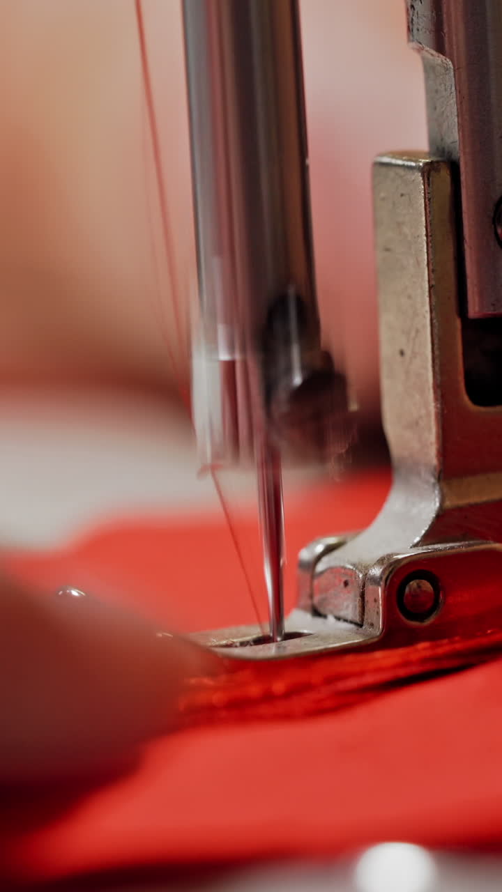 Process of sewing machine working with red fabric. Woman's hands at work on metal sewing machine with bright red material. Close-up Vertical video