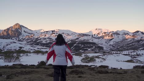 women in a winter clothing walking towards snow covered mountains at dusk