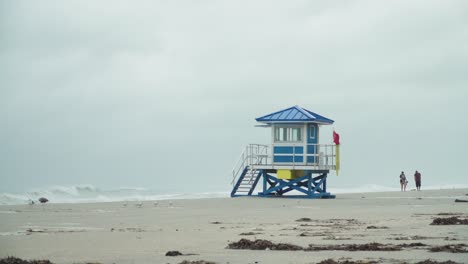 Tropensturm,-Rettungsschwimmerhaus-Mit-Roter-Fahne-Am-Leeren-Strand-An-Einem-Windigen-Und-Regnerischen-Tag