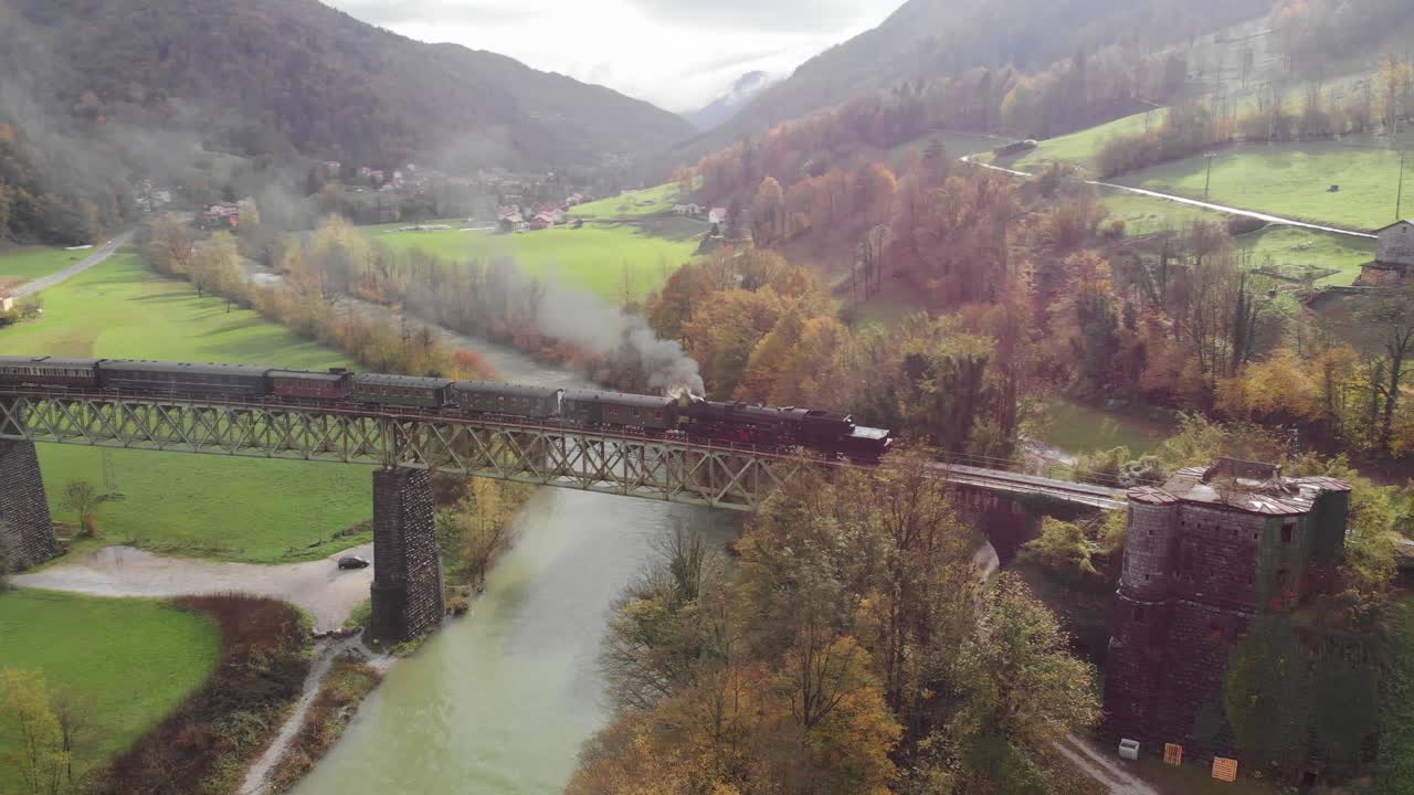 antigua locomotora de vapor con vagones que cruzan el puente ferroviario en el campo, el río fluye debajo, el humo proviene de los motores, el día nublado de finales de verano