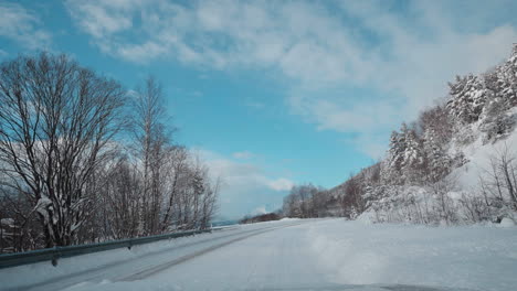 POV-video-of-a-daytime-drive-through-the-snowy-roads-of-Norway's-Western-Fjords,-surrounded-by-tall,-snow-covered-mountains-with-trees