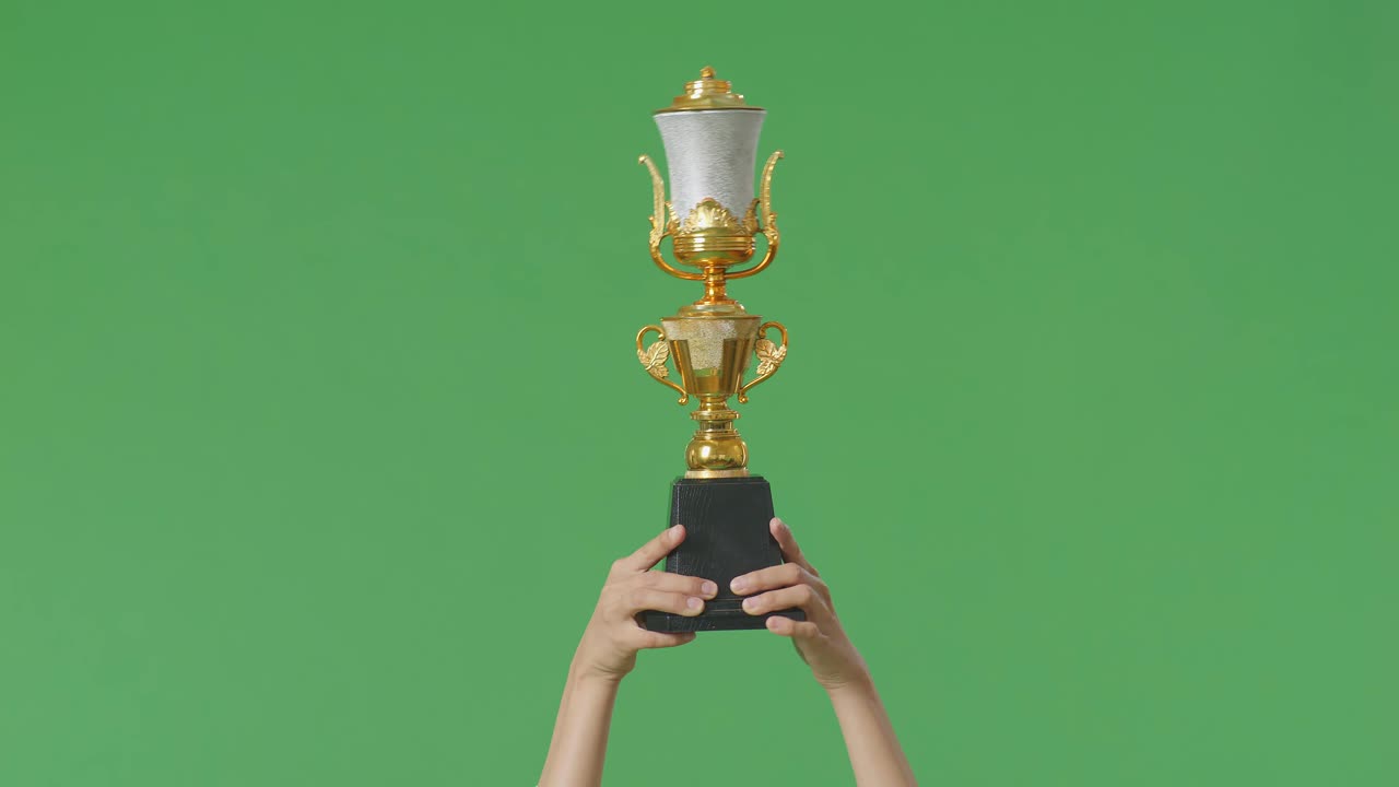 스튜디오의 녹색 스크린 배경에서 첫 번째 우승자로 우승을 축하하기 위해 공중에 금 트로피를 들고 있는 여성의 손