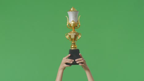 close up of female's hands holding a gold trophy up in the air to celebrate winning as the first winner on green screen background in the studio