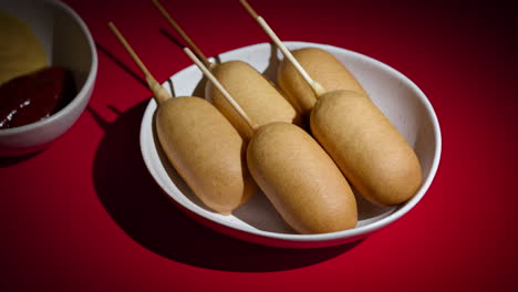 Side-shot-view-of-plate-with-five-corn-dogs-spinning-on-red-background.