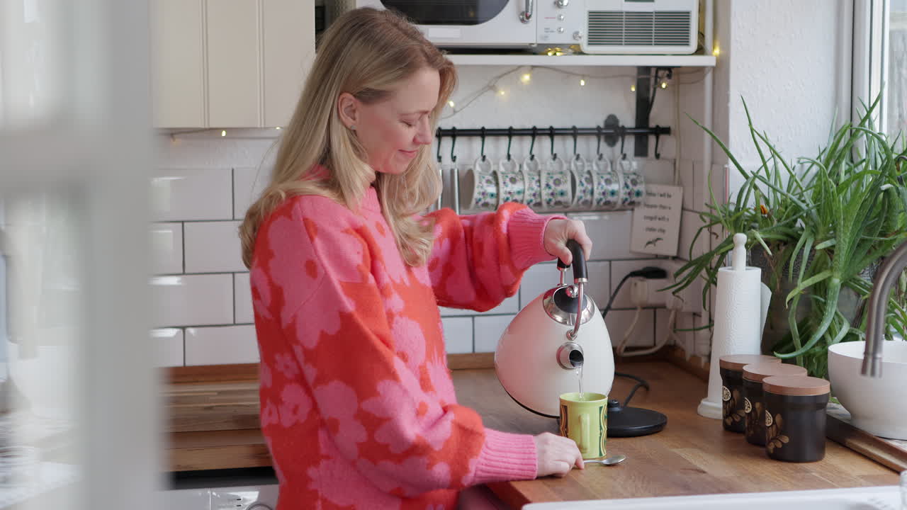 Woman pouring hot water from kettle into cup in the kitchen