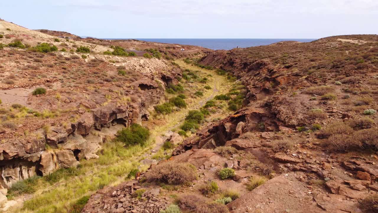 Carrellata aerea in avanti su un paesaggio desertico e arido di Tenerife con il mare sullo sfondo.