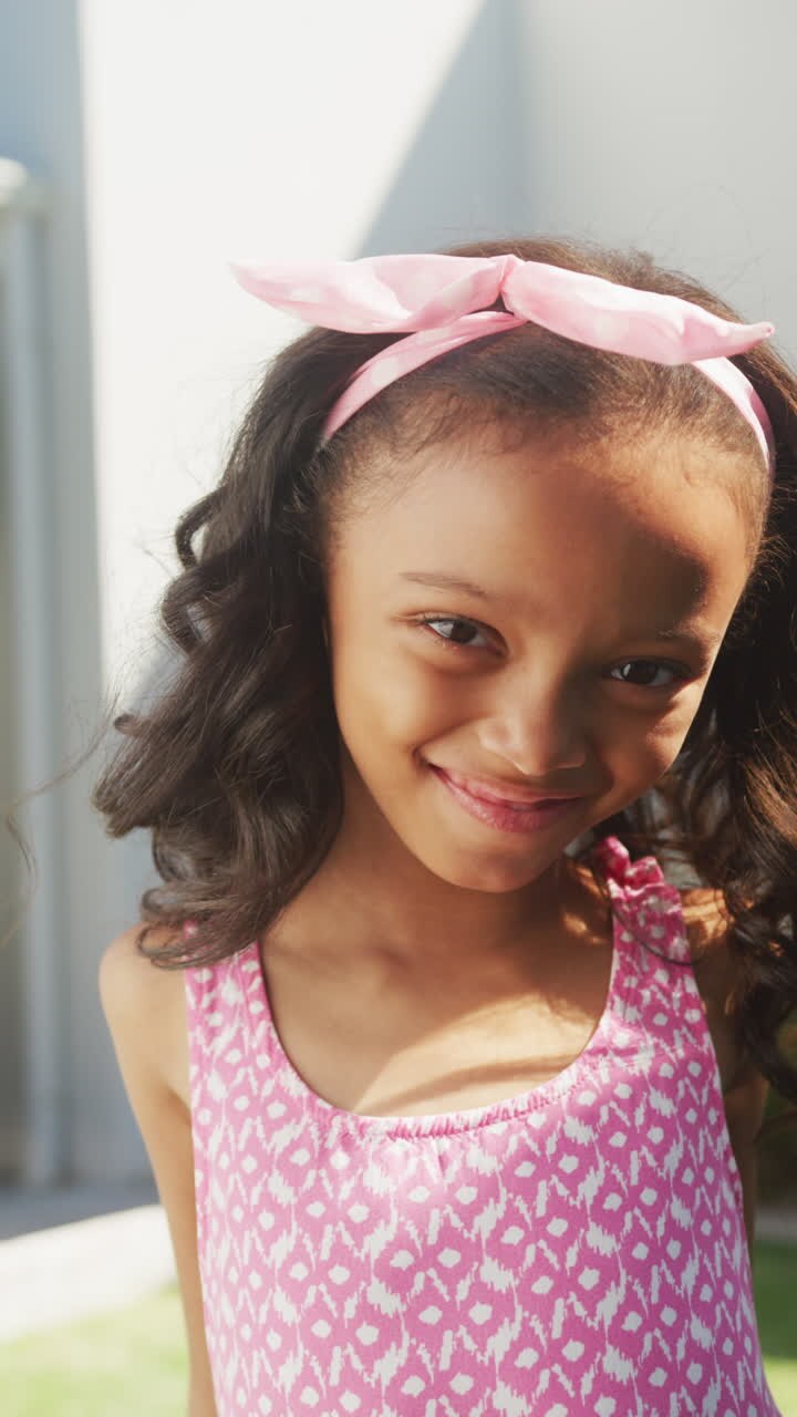 Retrato en video vertical de una niña afroamericana feliz sonriendo fuera de casa bajo la luz del sol