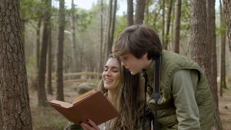 happy mother holding a book and her curious son reading it while exploring wildlife in a natural park