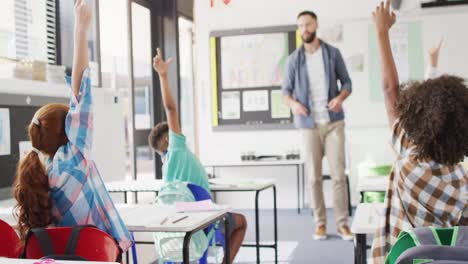 diverse male teacher and happy schoolchildren at desk in school classroom