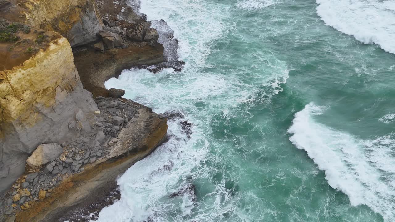 Drone captures dramatic cliffs and crashing waves along Port Campbell's coastline under overcast skies