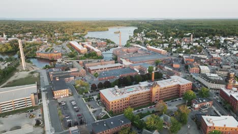 aerial view of downtown biddeford, maine featuring historic mill buildings, the saco river, and a vibrant small cityscape surrounded by forest and coastline.