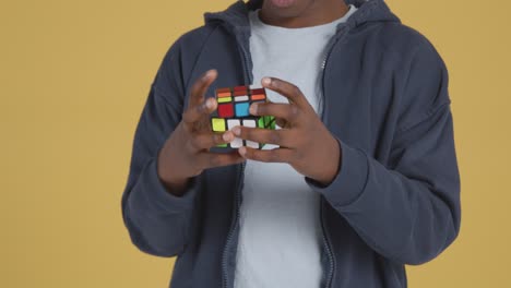 studio portrait of young boy on asd spectrum solving puzzle cube on yellow background