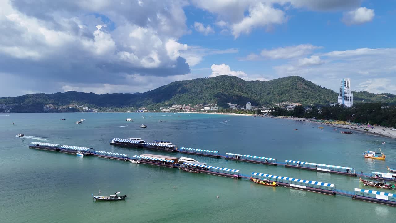 Drone footage captures boats and pontoons at Patong Beach, Phuket, under clear skies, showcasing vibrant coastal scenery