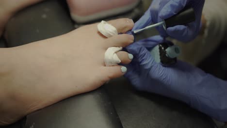 manicurist applying baby blue color nail polish on customer's toenail