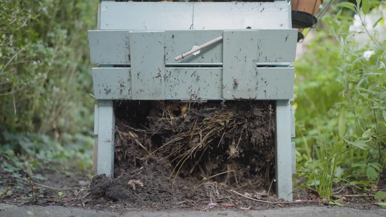 Close-up of a compost bin being opened, revealing decomposing organic material and soil formation process